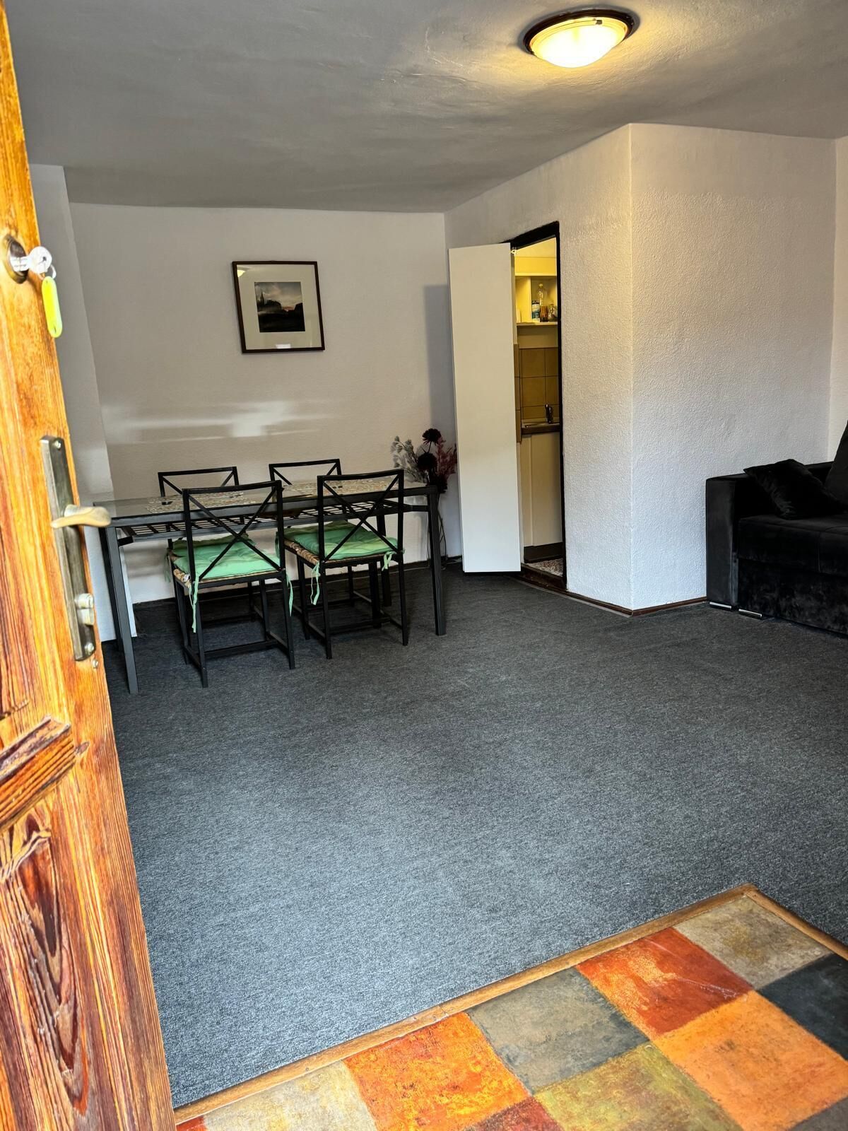 Une pièce comprenant une table à manger et des chaises, un canapé noir, un tableau encadré accroché au mur et une porte avec un cadre en bois.