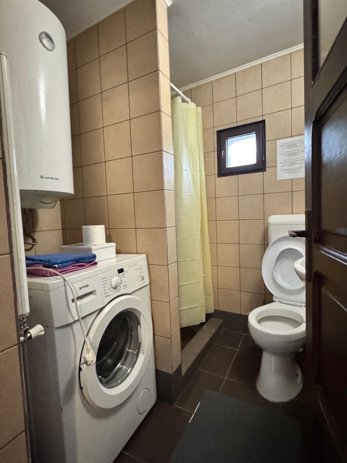 A compact bathroom with a washing machine, toilet, and a shower curtain.