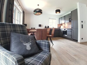 A modern kitchen with grey cabinets, a dining area with a table and chairs, and a plaid-patterned armchair with a deer pillow. - 6_ALP - Chalet Speiereck 4 by Interhome (Mariapfarr)
