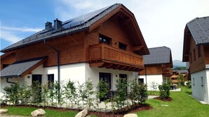 Una casa moderna de madera con balcón, rodeada por un jardín cuidado y un camino de entrada de grava.