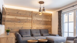 Una sala de estar moderna con un sofá modular, dos mesas auxiliares redondas de madera, un televisor montado en la pared y una ventana con cortinas.