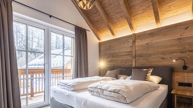 Un dormitorio con una cama grande, vigas de madera en el techo, una mesita de noche y vistas a un paisaje nevado.