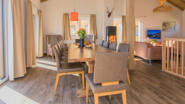 Un amplio salón con techo de madera, chimenea, mesa de comedor con sillas y televisor.