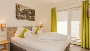 Habitación de hotel con cama, mesita de noche, lámpara de pared, ventana con persianas y puerta con cortina.