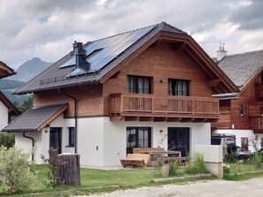 A wooden chalet with a balcony, a solar panel, and a car parked outside. - 6_ALP - Chalet Speiereck 6 by Interhome (Mariapfarr)