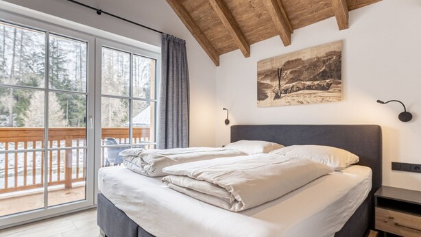 Une chambre avec un grand lit, un plafond en bois, une fenêtre donnant sur les arbres et un tableau accroché au mur.