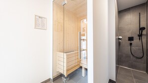 Une salle de bain moderne avec un sauna en bois, une douche en verre et un sol carrelé.