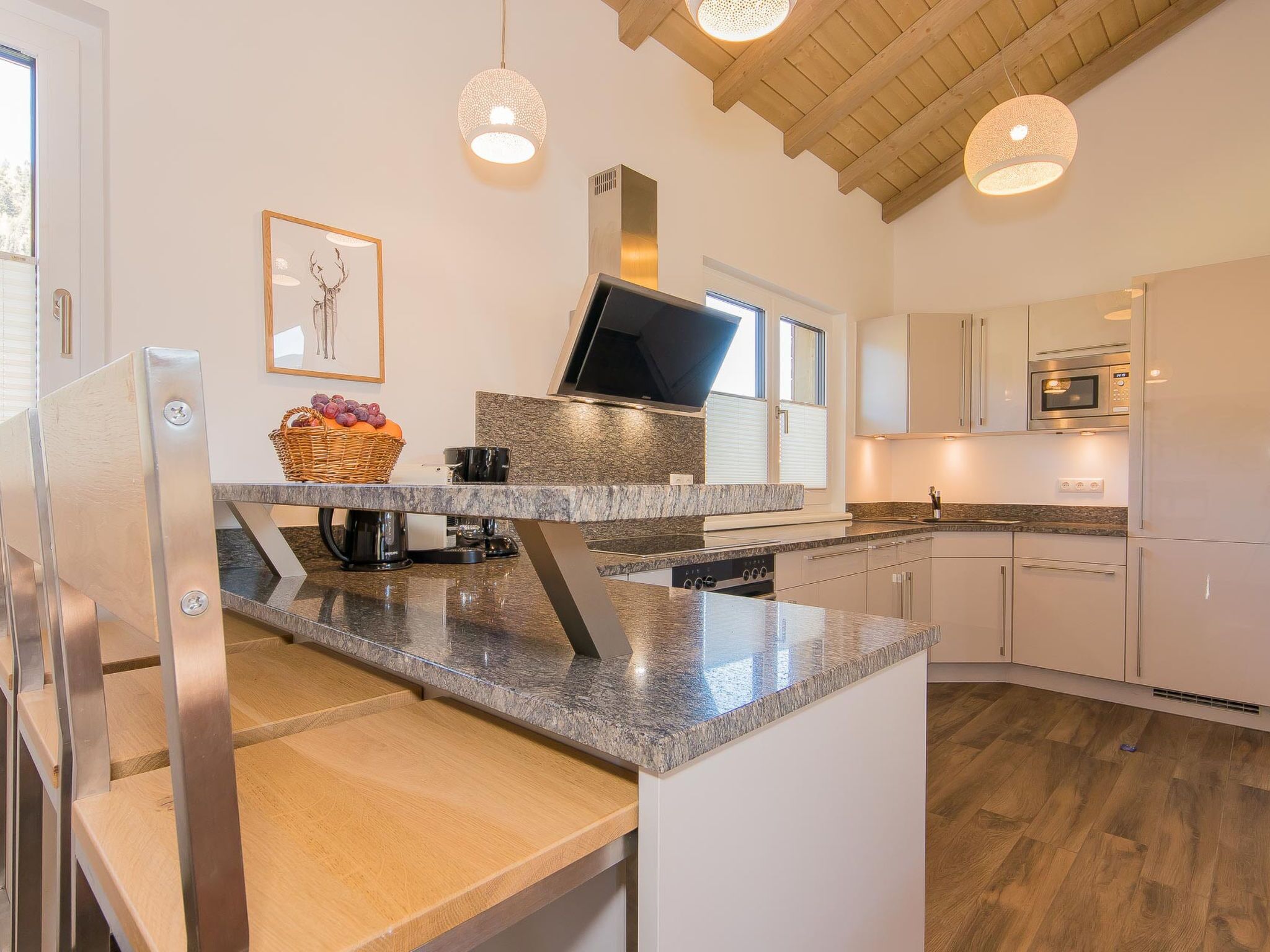 Une cuisine moderne dotée de plans de travail en granit, d’appareils électroménagers en acier inoxydable et de luminaires suspendus.