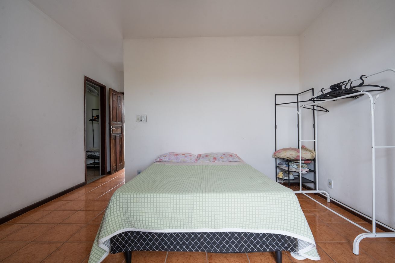 Une petite pièce propre, avec un lit simple, un étendoir métallique et une porte donnant sur une autre pièce.