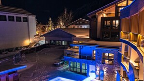 Un edificio moderno con piscina, mobiliario exterior y una entrada bien iluminada.