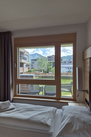 A hotel room with two beds, a large window with a view of buildings and greenery, and a wooden door. - 3_SPA - Deluxe Garden 417 by Interhome (Zell am See)