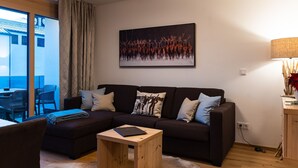 A modern living room with a dark sofa, a small wooden side table, and a large window with curtains. - 3_SPA Deluxe Garden 417 by Interhome (Zell am See)