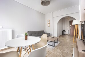 A modern living room with a round dining table, a grey sofa, and a TV stand with a lamp. - City Center Calm Spot (Glifada)