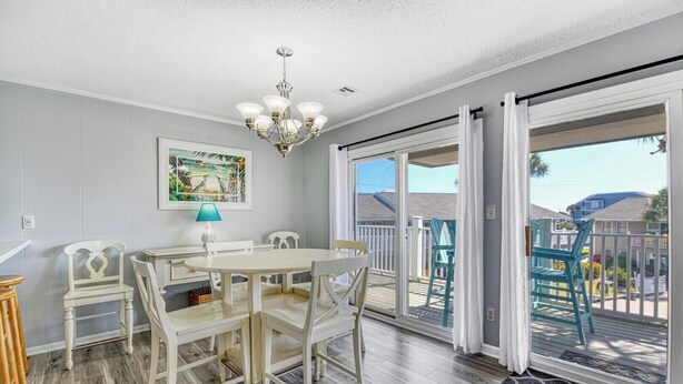 A dining area with a table and chairs, a chandelier, a painting, and a view through a sliding glass door to the outside. - Floral Villa D14 - Three Bedroom Two Bath Condo with Shared Pool (Surfside Beach)