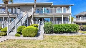 A two-story building with a central staircase, a balcony on the upper floor, and a well-maintained lawn with trimmed bushes. - Floral Villa D14 - Three Bedroom Two Bath Condo with Shared Pool (Surfside Beach)