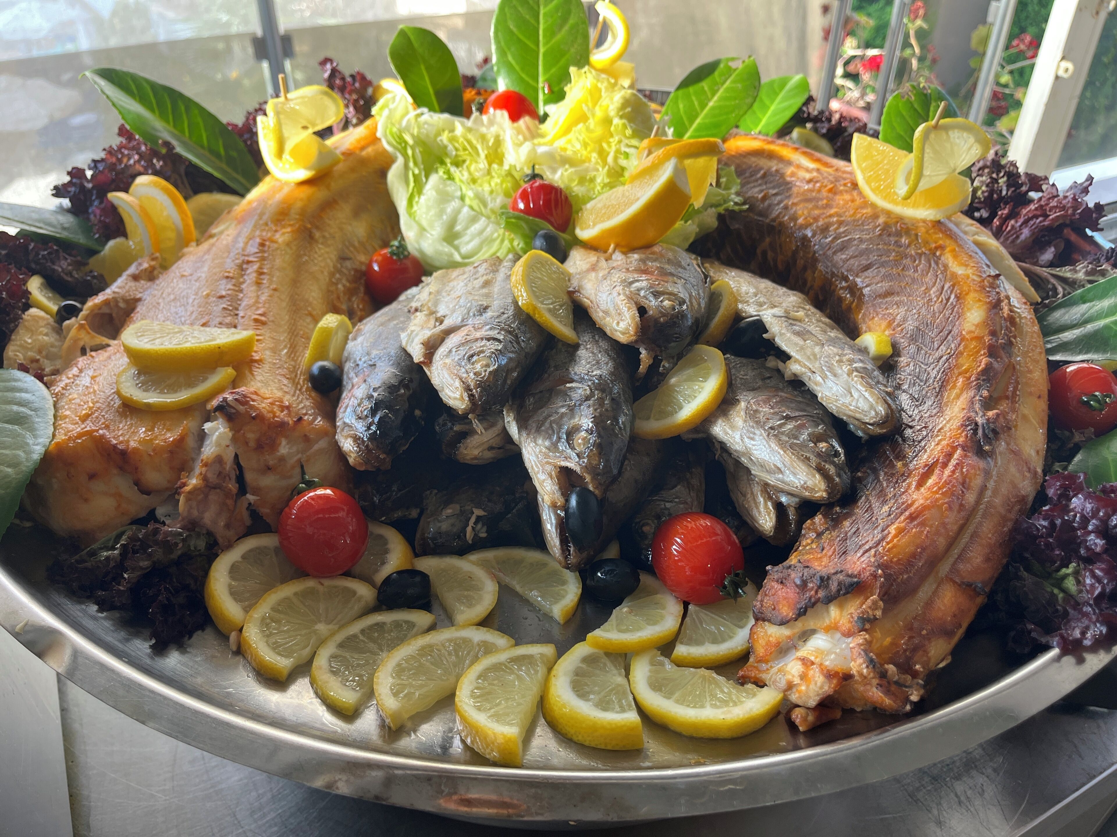 Una bandeja con pescado y verduras cocinadas, adornada con rodajas de limón y tomates cherry.