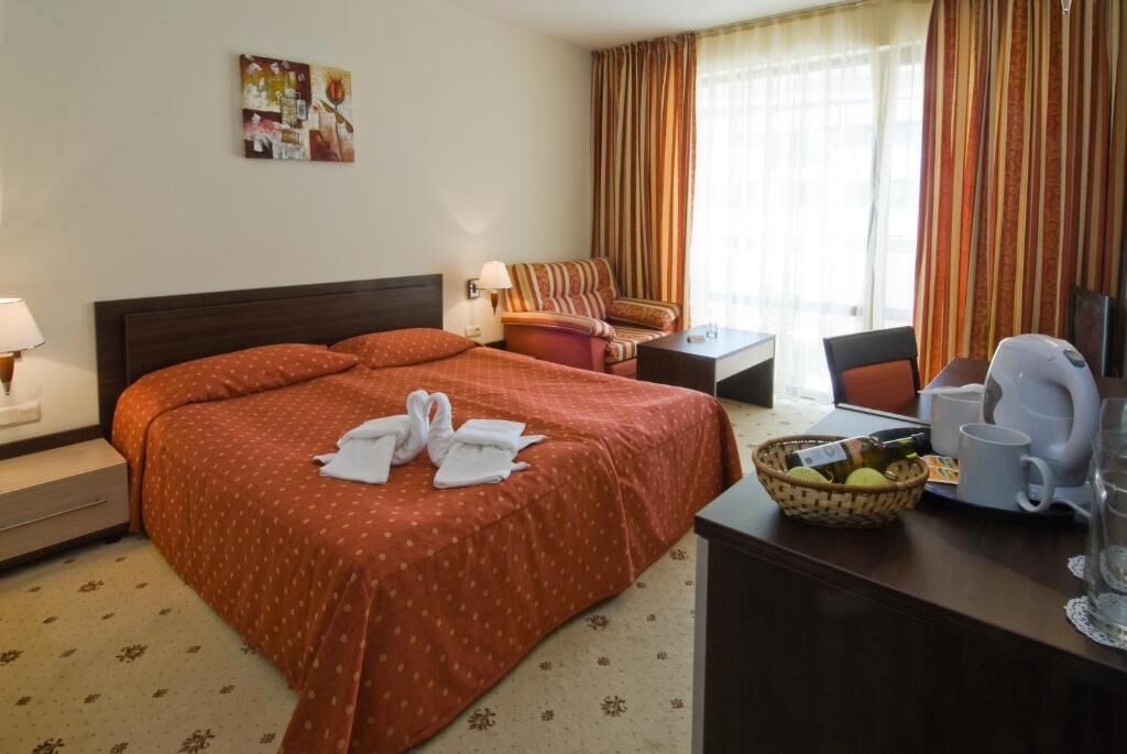 A hotel room with a large bed, a desk with a basket of fruit, a coffee maker, and a chair.