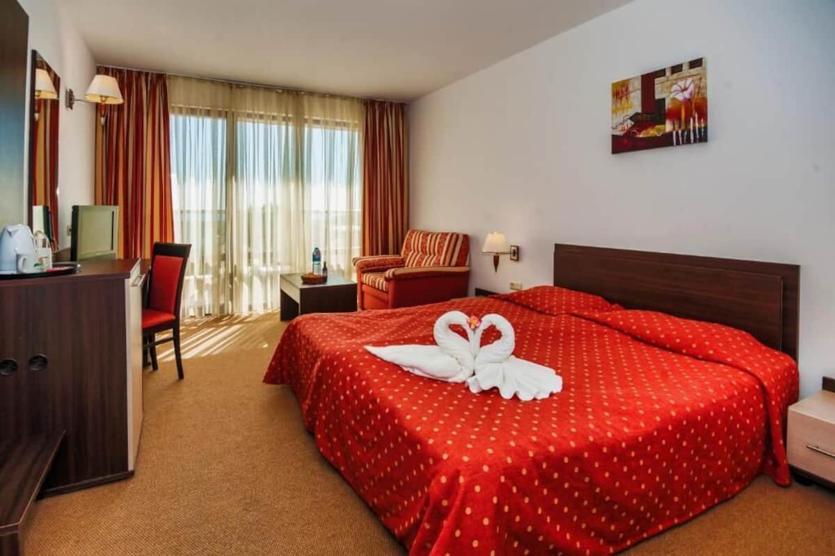Une chambre d’hôtel avec un lit, un bureau, une chaise, une table de chevet et un tableau au mur.