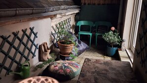 A narrow outdoor space with a wooden bench, potted plants, and a tiled floor.