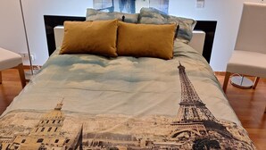 A bed with a cityscape and Eiffel Tower design, two pillows, and a large abstract painting on the wall.