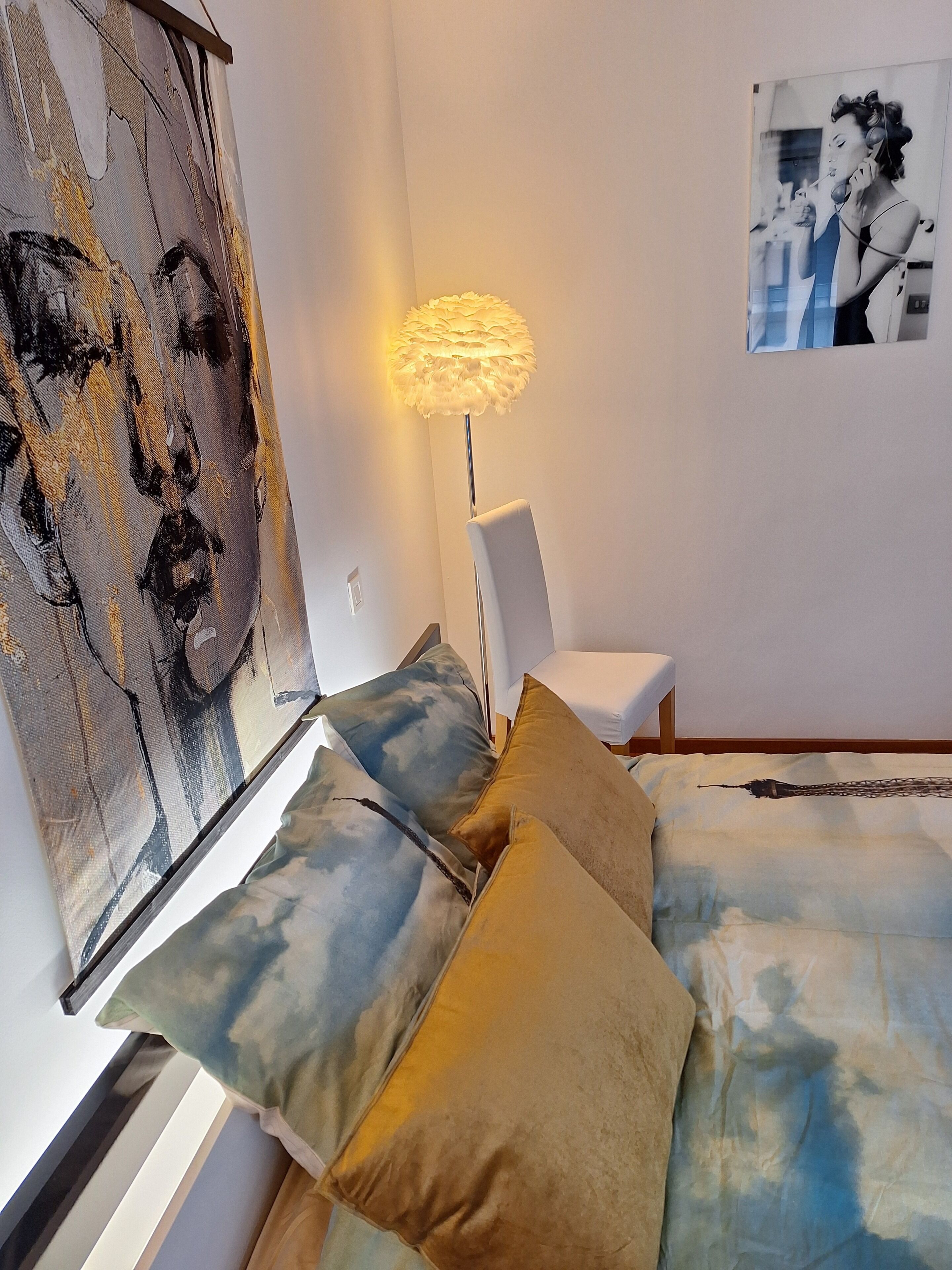 Un dormitorio con cama, almohadas, lámpara y una obra de arte en la pared.