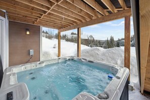 Ein Whirlpool mit Holzboden und Blick auf eine verschneite Landschaft.