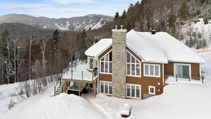 A two-story chalet with a ski lift, surrounded by snow-covered trees and mountains. - Waterfront with Spa - Pool Table - Le Rivage Alpin (Saint-Côme)