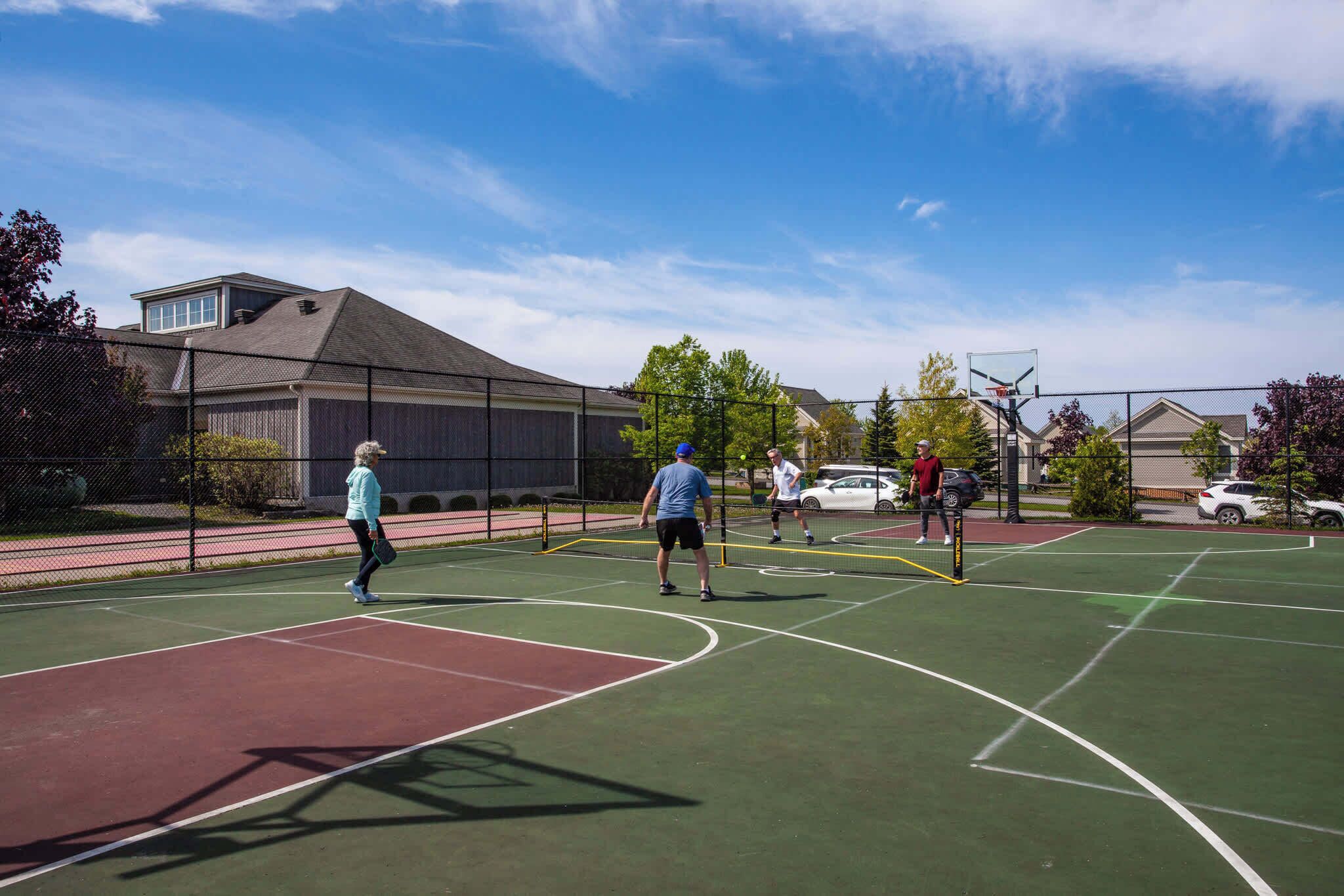 An outdoor basketball court with a net, surrounded by a fence, and adjacent to residential buildings.