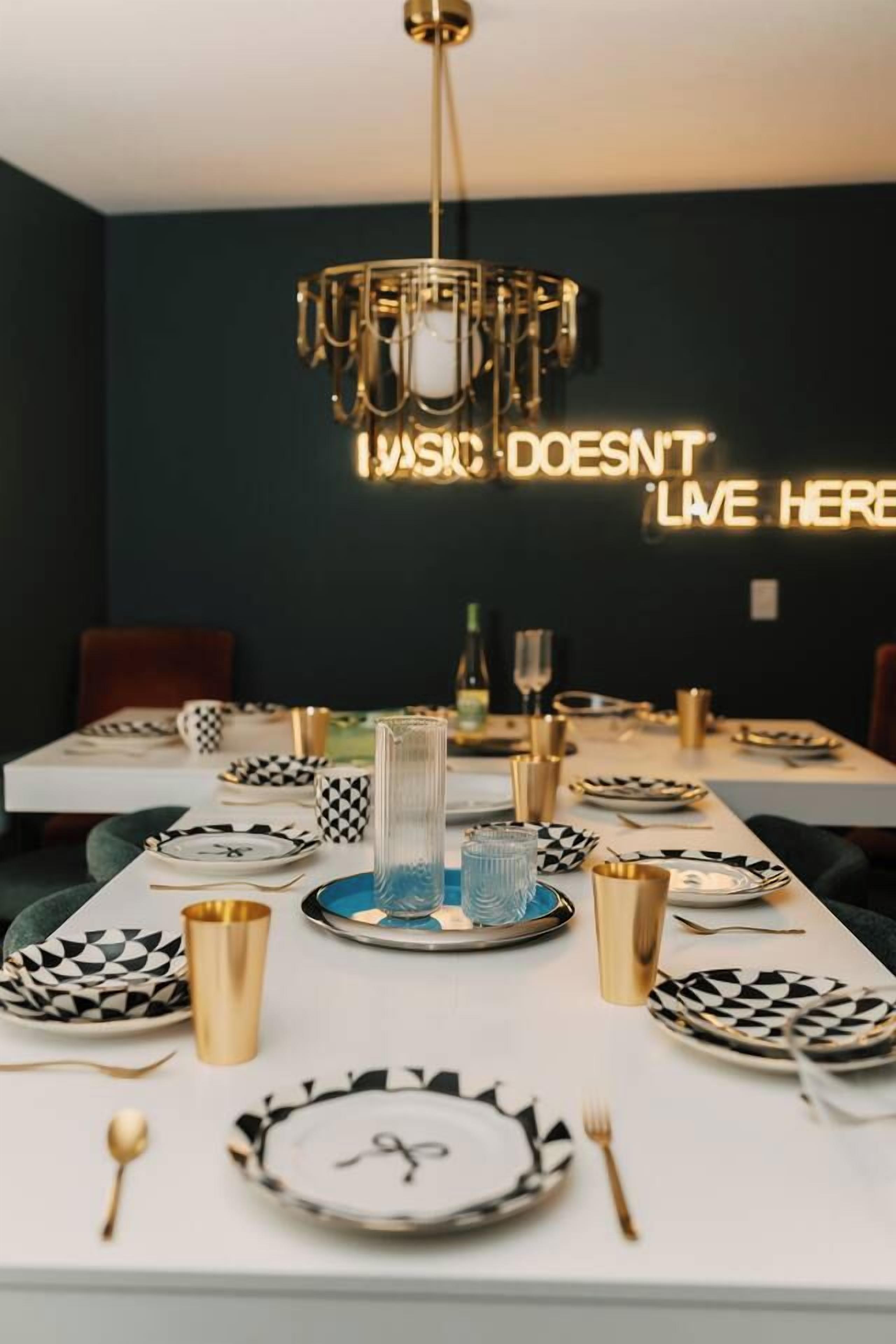 A dining table set with black and white patterned plates, gold cutlery, and a modern chandelier.
