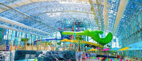 An indoor water park with a large green slide, multiple water slides, and a glass ceiling.