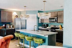 Une cuisine moderne dotée d’un îlot central, de tabourets de bar, d’appareils électroménagers en acier inoxydable et de luminaires suspendus.