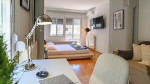 Et moderne hotelværelse med skrivebord, lampe, seng og fjernsyn på væggen.
