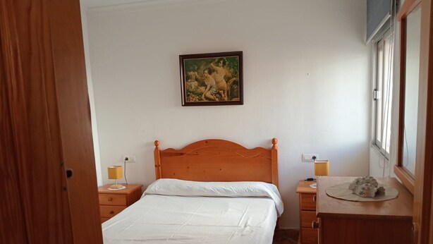 Ein Schlafzimmer mit einem hölzernen Bett, einem Nachttisch mit Lampe, einer Kommode und einem Gemälde an der Wand.