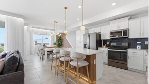 A modern kitchen with white cabinets, stainless steel appliances, and a central island with bar stools. - Storey Lake brand new near Disney lake & club view (Kissimmee)
