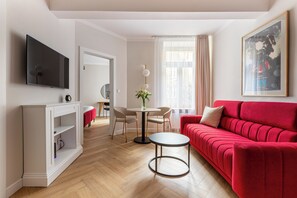 A modern living room with a red sofa, a TV, a dining area with chairs, and a small table. - Native Apartments Potebni 8 (Kraków)