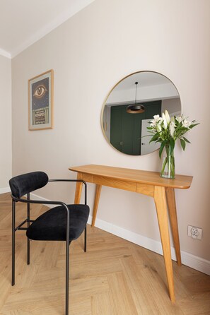 A room with a wooden desk, a black chair, a round mirror, and a vase with flowers. - Native Apartments Potebni 8 (Kraków)