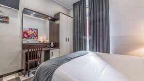 A hotel room with a bed, a desk with a chair, a painting on the wall, and a window with curtains. - Rome in Love B&B - Termini Train Station (Rome)