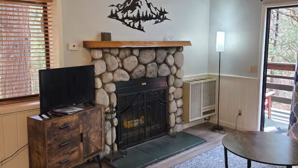 A living room with a stone fireplace, wooden ceiling, and a TV on a wooden cabinet.