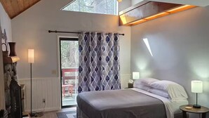 A bedroom with a bed, bedside lamps, a desk, a chair, a window with curtains, and a skylight. - Cozy Studio in Idyllwild (Idyllwild-Pine Cove)