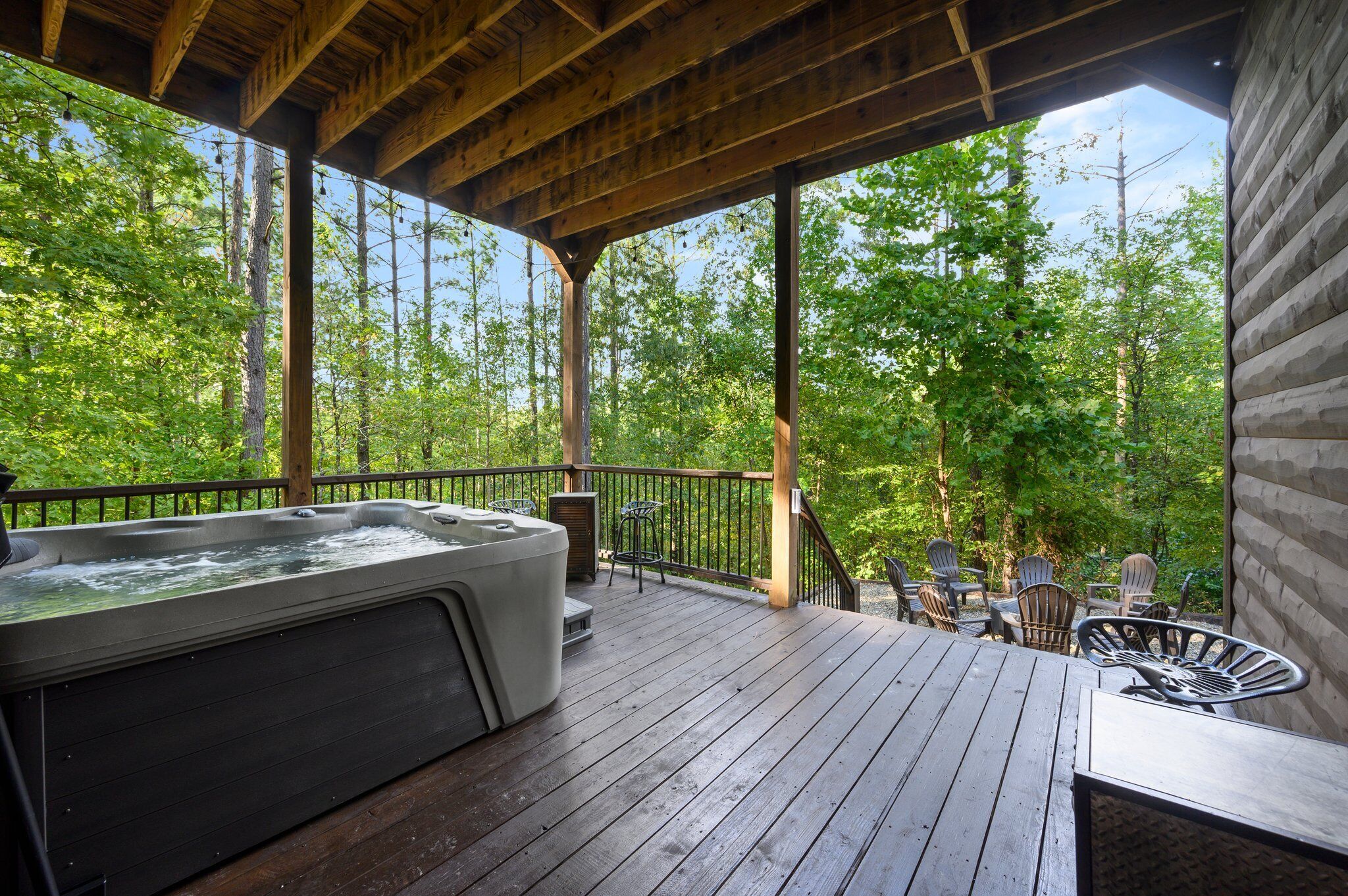 A wooden deck with a hot tub, outdoor seating, and a view of a forest.