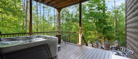 A wooden deck with a hot tub, outdoor seating, and a view of a forest.