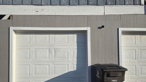 Ett hus med två garageportar, en soptunna och ett fönster med fönsterluckor.
