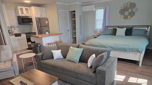 Ett kompakt bostadsutrymme med ett litet kök, en soffa, en säng och en liten matplats.