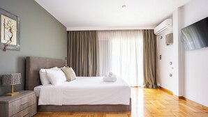 A modern bedroom with a large bed, a nightstand, a lamp, and a flat-screen TV. - Charming Maisonette In Southern Suburbs (Voula)