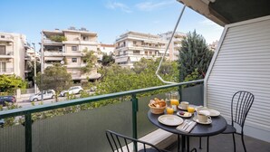 A balcony with a table set for breakfast, a view of residential buildings, and a green fence. - Charming Maisonette In Southern Suburbs (Voula)