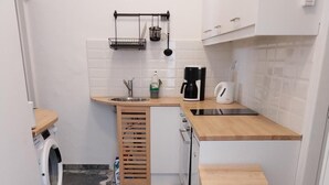 A compact kitchen with a washing machine, a sink, a coffee maker, and a wooden stool. - Apartment 'I Have A Dream' with Sea View, Private Terrace and Air Conditioning (Agia Pelagia)