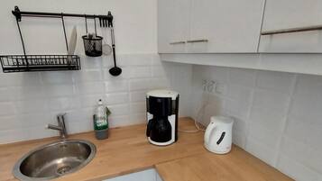 Une cuisine équipée d’un évier, d’une machine à café, d’une bouilloire et d’une horloge murale.