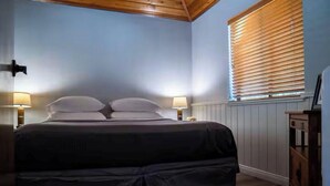 Een slaapkamer met een bed, twee bedlampen, een raam met zonwering en een houten plafond.