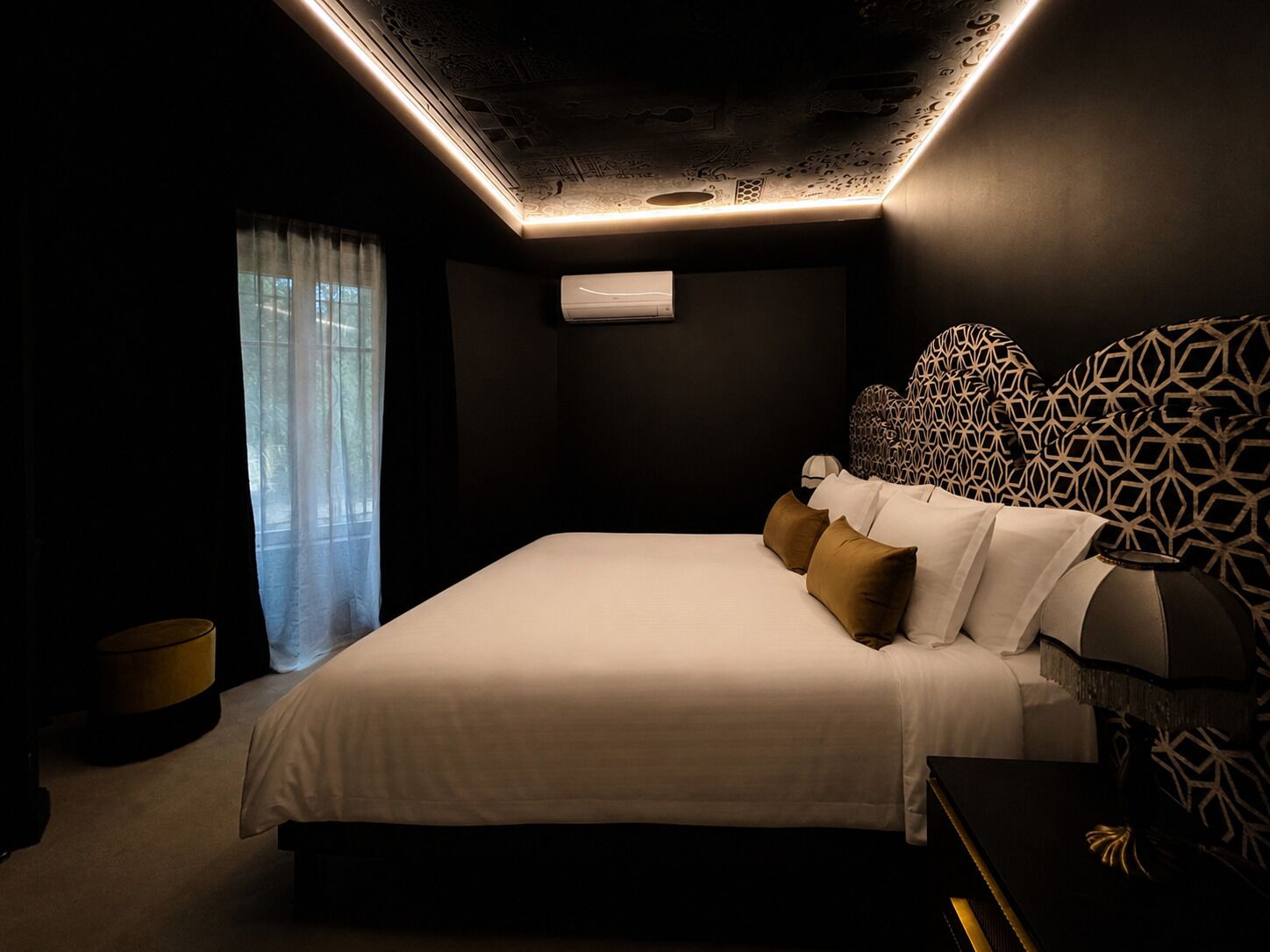 Een moderne slaapkamer met een bed, een hoofdbord met patroon en een plafondlamp.