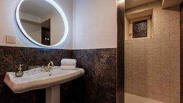 Ein Badezimmer mit rundem Spiegel, einem weißen Waschbecken und einer Dusche mit gemusterten Fliesen.